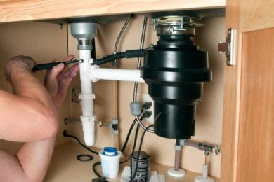 Plumber repairing a garbage disposal beneath a kitchen sink in Philadelphia